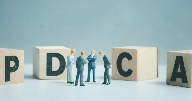PDCAブロックの前で話し合う四人の人形。利用状況を可視化してAI活用を改善するイメージ