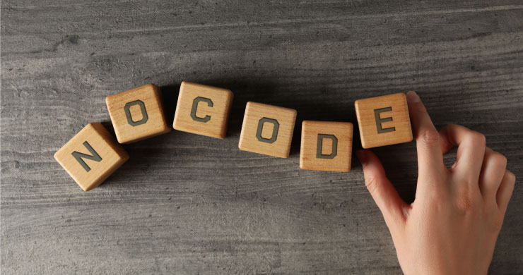 アルファベットの書かれた木製キューブが並び、手がEのキューブを置いて『NOCODE』と読める。直感的にAIを構築できるノーコードツールを表現。