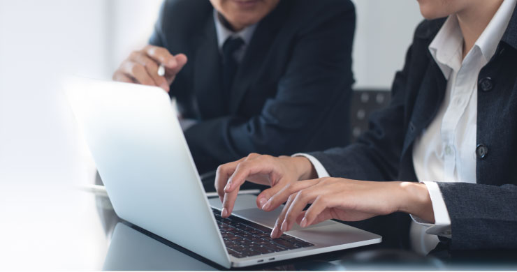 ビジネスマン2人がPCを前に相談し、担当者が助言する様子。社内リソース不足でもテンダがJUST.DB開発と奉行クラウド連携を柔軟に支援するイメージ。