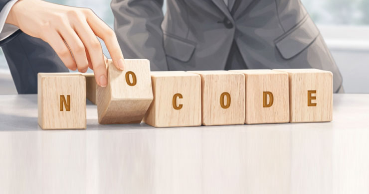 木製キューブで「NOCODE」の文字が完成していく様子が、紙帳票に頼っていた現場がノーコードで自ら業務を改善し、成果を生み出していく変革の過程を象徴しているイメージ